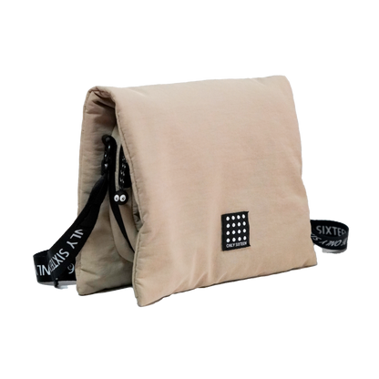 Beige pillow with black straps and branding on a white background